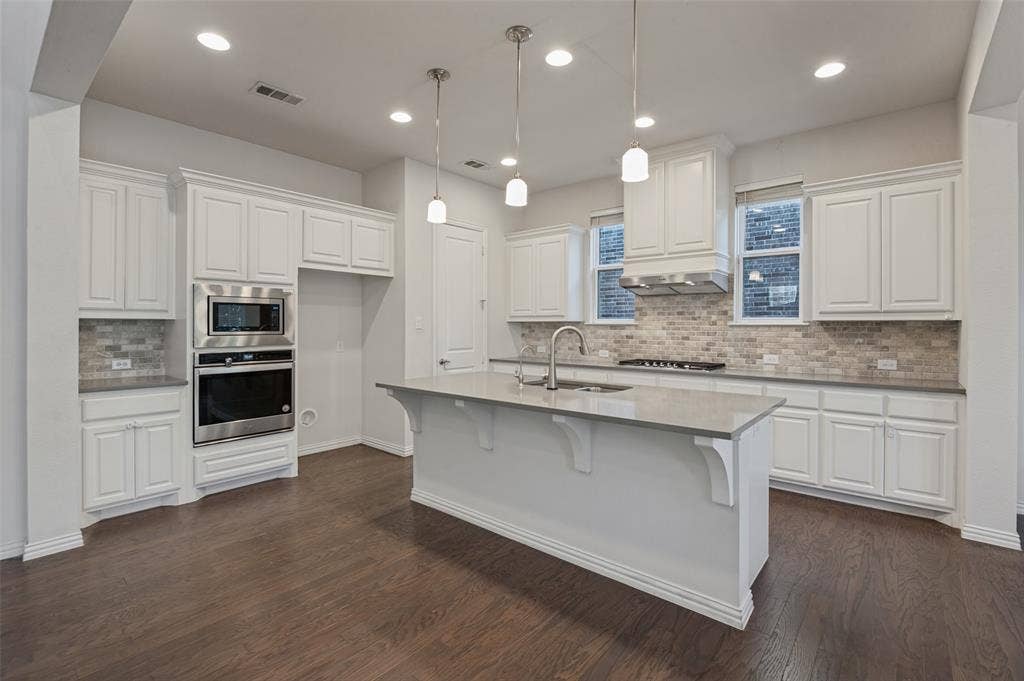 Kitchen featuring white cabinetry, center island with stone-composite countertop, stainless steel built-in double oven, wood-finish flooring, and recessed lighting