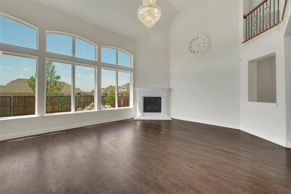 302 Torch Lily Lane, Wylie, TX 75098 Vaulted ceiling with an elegant chandelier, wood-finish flooring, a fireplace with a white mantel, and a wall of arched windows