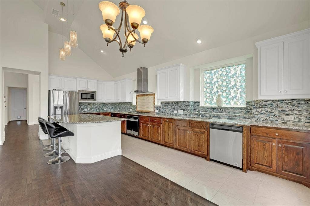 302 Torch Lily Lane, Wylie, TX 75098 Vaulted ceilings, a kitchen island with granite countertops, stainless steel appliances, white upper cabinetry, and wood-finish lower cabinetry