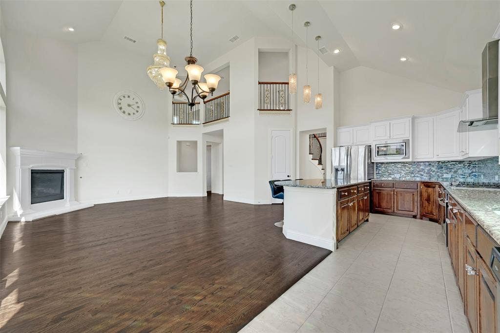 302 Torch Lily Lane, Wylie, TX 75098 Vaulted ceilings with recessed lighting, a corner fireplace with a white mantel, wood-finish flooring, and a kitchen island with built-in cabinetry