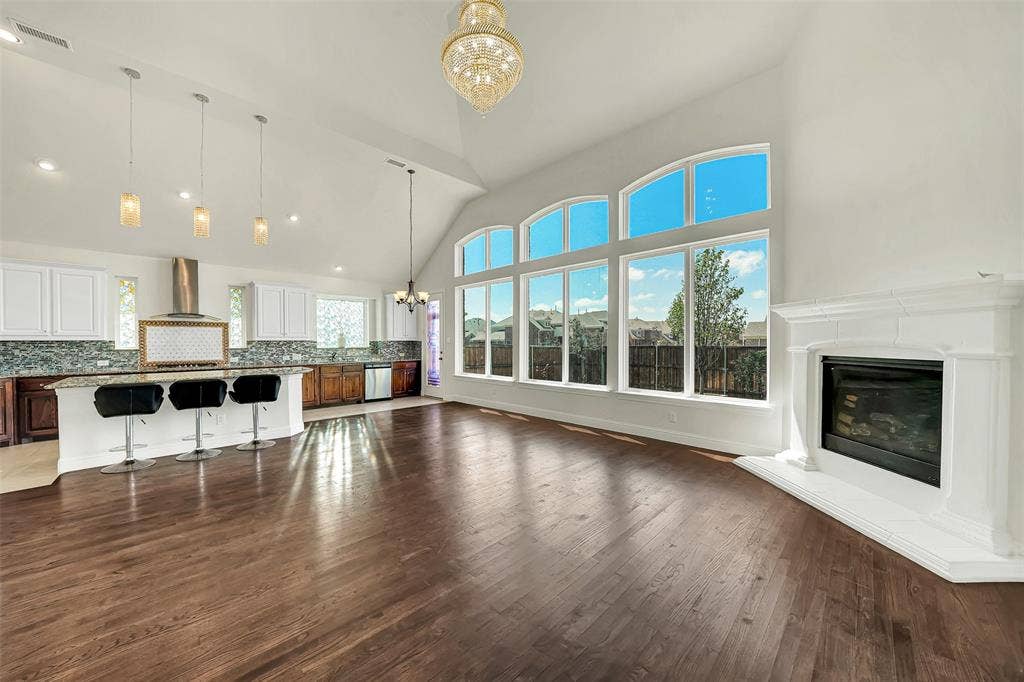 302 Torch Lily Lane, Wylie, TX 75098 Vaulted ceiling with an ornate chandelier, expansive window wall with arched transoms, wood-finish flooring, and a corner fireplace