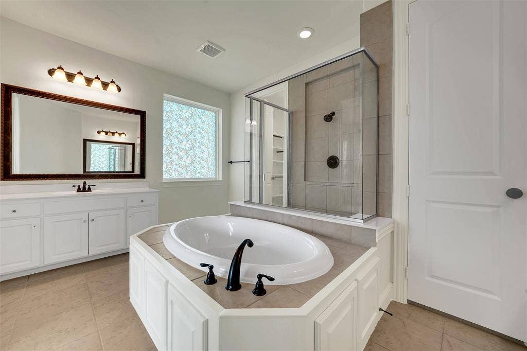 302 Torch Lily Lane, Wylie, TX 75098 Bathroom featuring a built-in soaking tub with dark-finish fixtures, a glass-enclosed shower, a double vanity with a rectangular mirror, and light-tone floor tiling