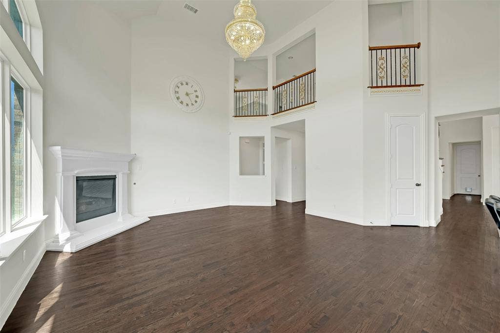 302 Torch Lily Lane, Wylie, TX 75098 Hardwood flooring throughout, two-story ceiling, decorative chandelier, corner fireplace, and upper-level interior balconies with wrought iron railings