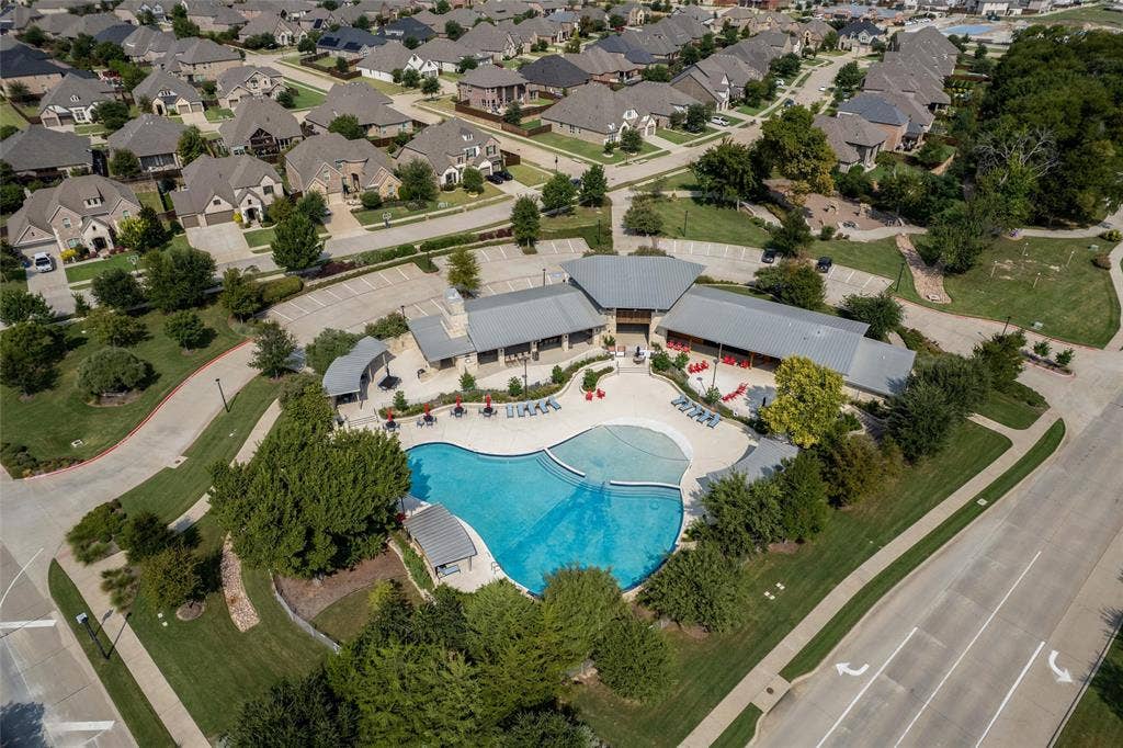 7601 Calhoun Cove, McKinney, TX 75071 Expansive community pool with curved edges, adjacent clubhouse structures with gabled roofs, surrounding green spaces, and paved parking areas
