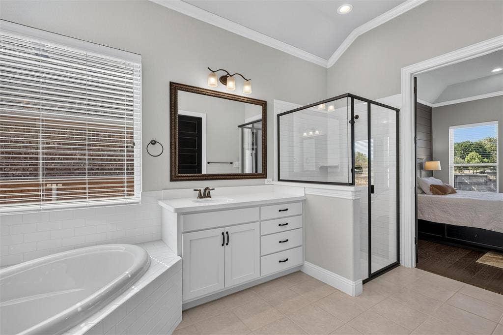 7601 Calhoun Cove, McKinney, TX 75071 White shaker vanity with quartz countertop, walk-in shower with black frame, soaking tub with white tile surround, and vaulted ceiling