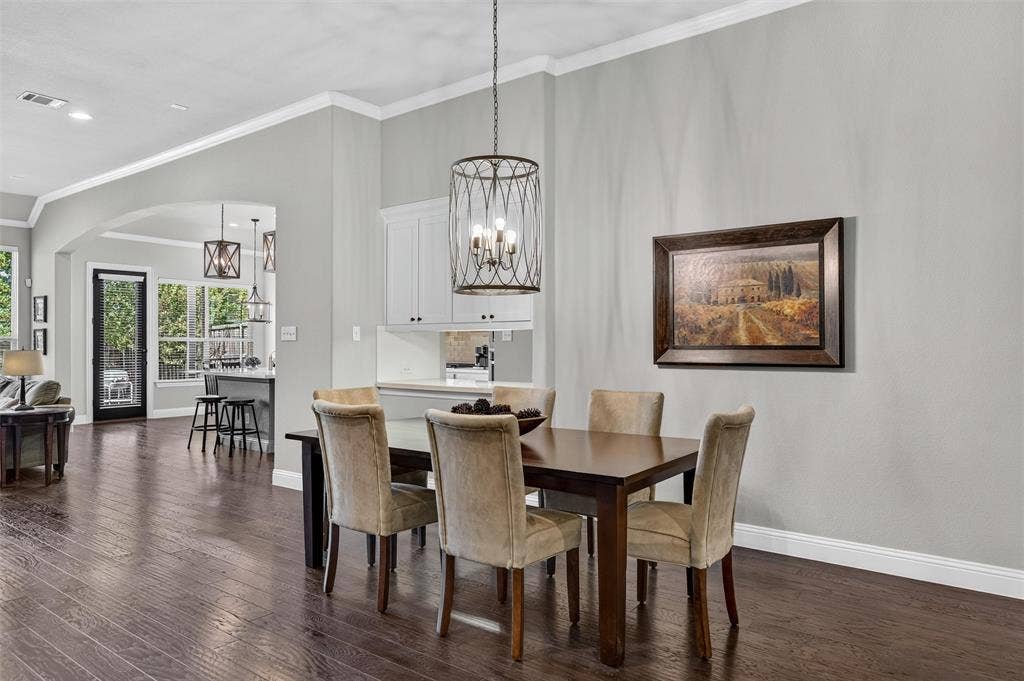 7601 Calhoun Cove, McKinney, TX 75071 Dark wood-finish flooring, crown molding, arched entryway, white cabinetry, and a drum pendant light fixture