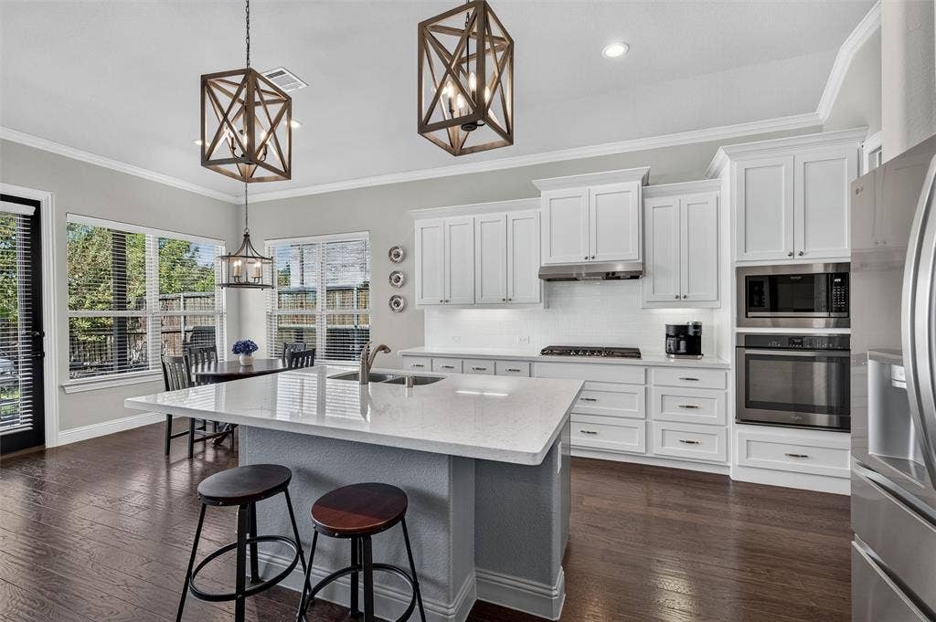 7601 Calhoun Cove, McKinney, TX 75071 Kitchen featuring a white quartz-finish island, dark wood-finish flooring, white cabinetry, stainless steel appliances, and multiple windows