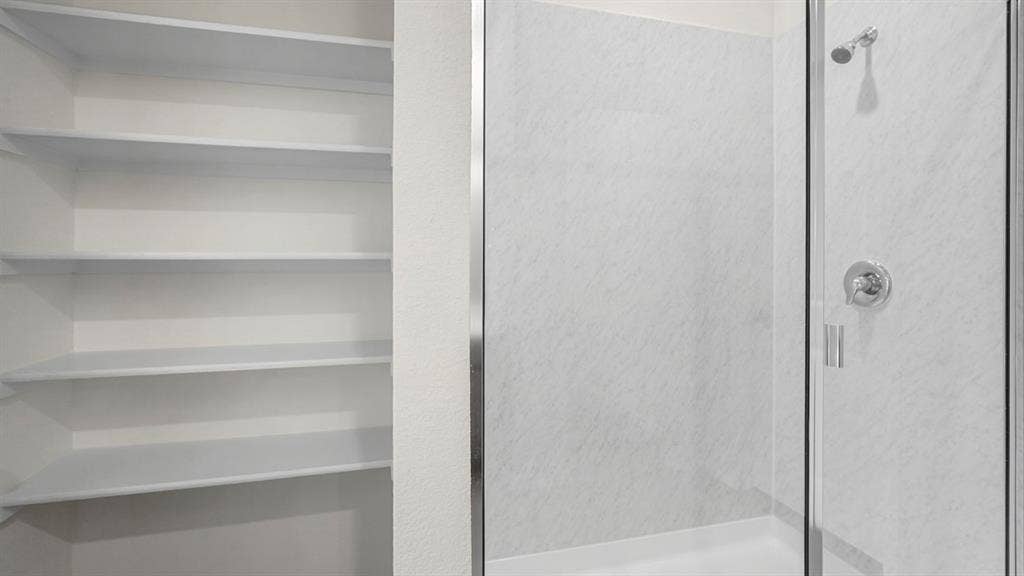 1671 Blaire Drive, Tyler, TX 75702 Built-in shelving, shower with clear glass enclosure, chrome showerhead, and chrome control handle
