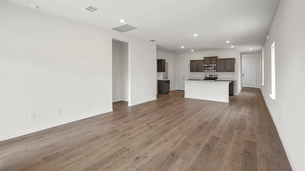 1671 Blaire Drive, Tyler, TX 75702 Open-concept space featuring wood-finish flooring, recessed lighting, white walls, and a kitchen with dark cabinetry, white countertops, and stainless steel appliances