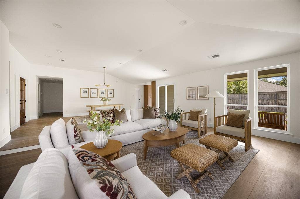 Bright and inviting living area featuring vaulted ceilings, a beautifully updated brick fireplace with wood mantel, built-in shelving, and large windows overlooking the backyard.