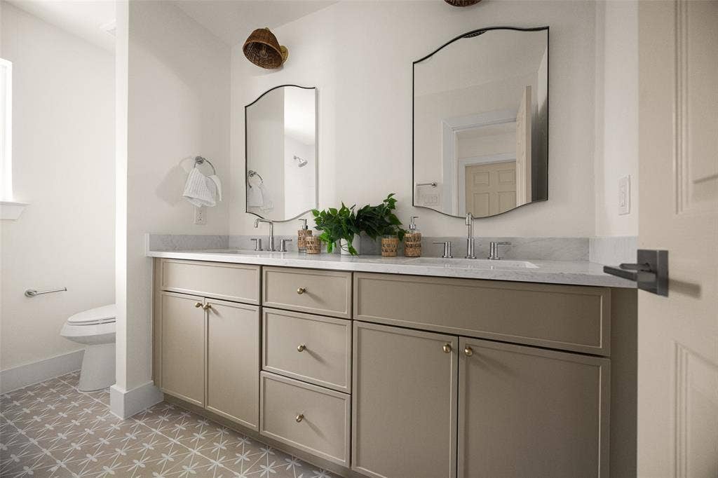 Fully updated secondary bathroom featuring a double vanity, refined finishes, decorative tile flooring, and a bright tub-shower surround with clean, timeless tilework.