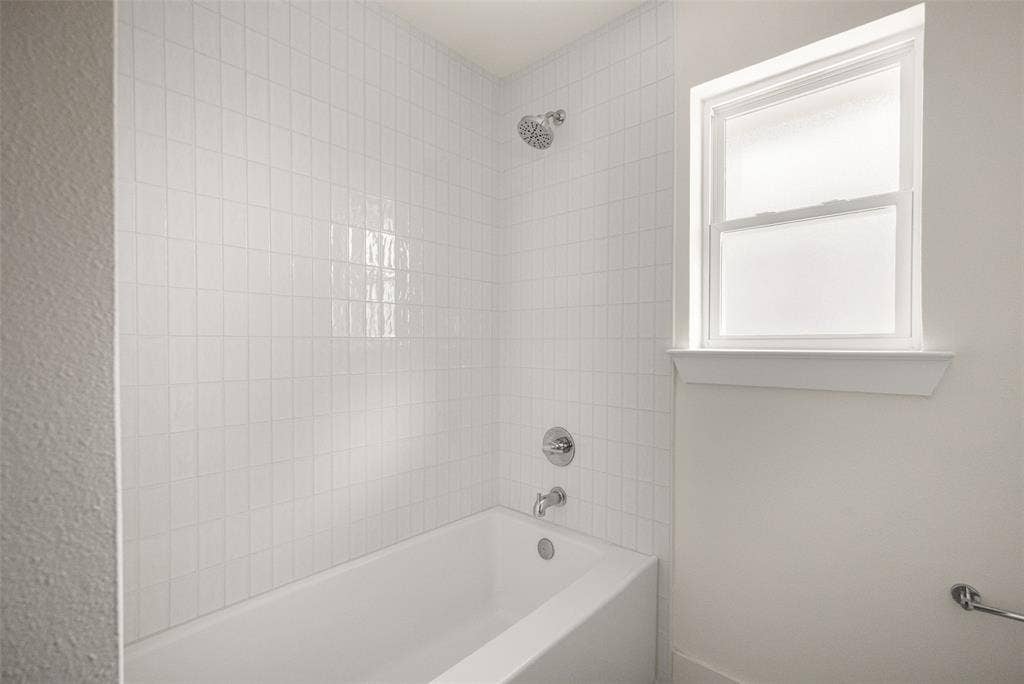 Fully updated secondary bathroom featuring a double vanity, refined finishes, decorative tile flooring, and a bright tub-shower surround with clean, timeless tilework.