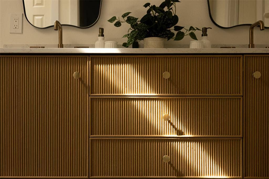 Luxuriously updated primary bathroom featuring a striking fluted wood double vanity, elegant brass fixtures, and designer mirrors.