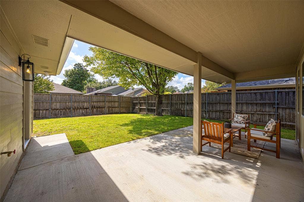 Covered patio with generous space for outdoor seating and dining, overlooking the fenced backyard and mature shade tree.
