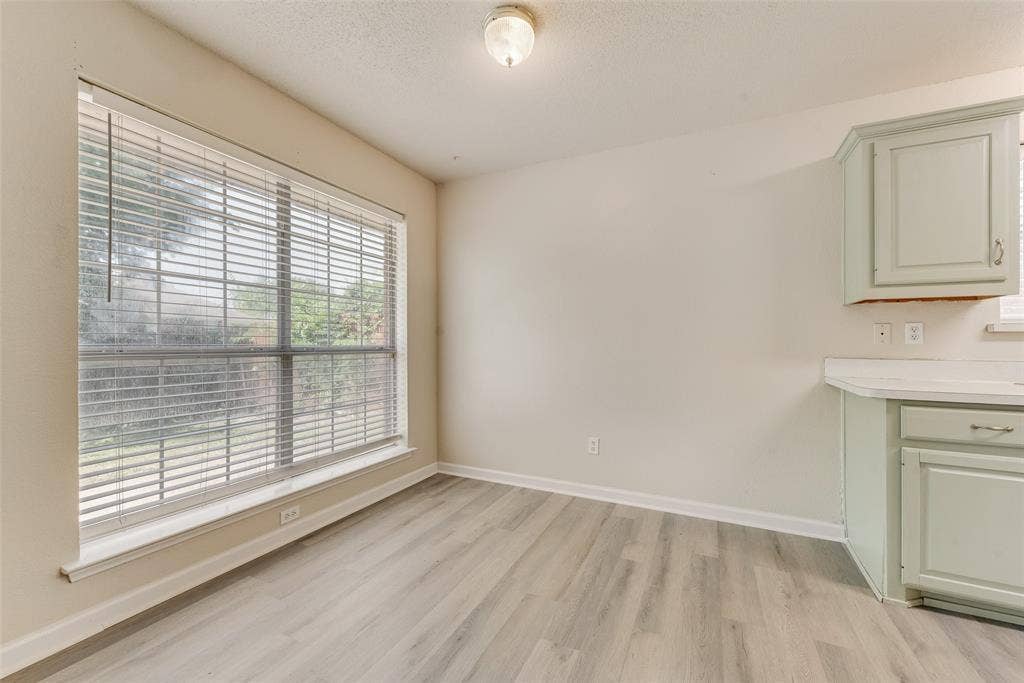220 Hollywood Drive, Glenn Heights, TX 75154 Light wood-finish flooring, a large window with horizontal blinds, built-in cabinetry with hardware, and solid surface countertops
