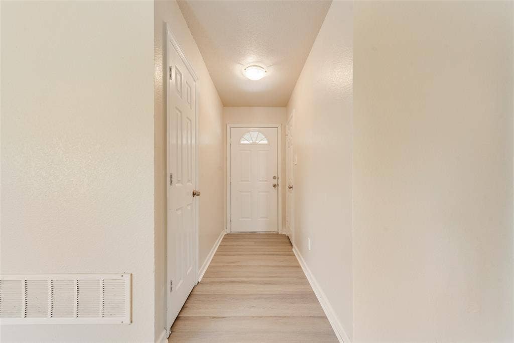220 Hollywood Drive, Glenn Heights, TX 75154 Hallway featuring neutral wall tones, wood-finish flooring, a paneled interior door, and a white exterior door with an arched glass insert