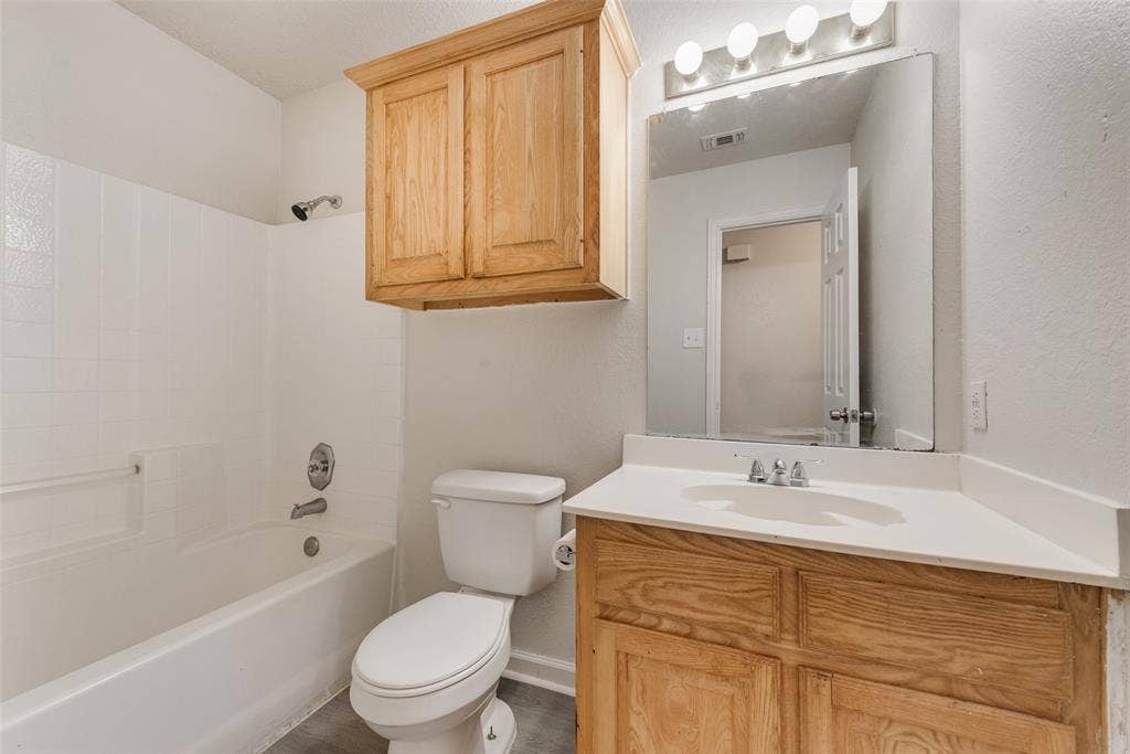 220 Hollywood Drive, Glenn Heights, TX 75154 White tub/shower combination, wood-finish vanity with an integrated sink, and overhead wood-finish cabinetry