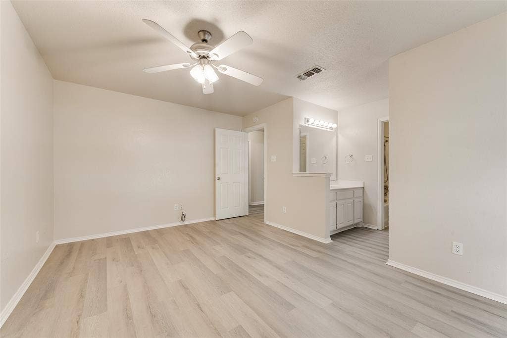 220 Hollywood Drive, Glenn Heights, TX 75154 Spacious room with light wood-finish flooring, ceiling fan, and access to a vanity area with built-in cabinetry, a rectangular mirror, and vanity lighting