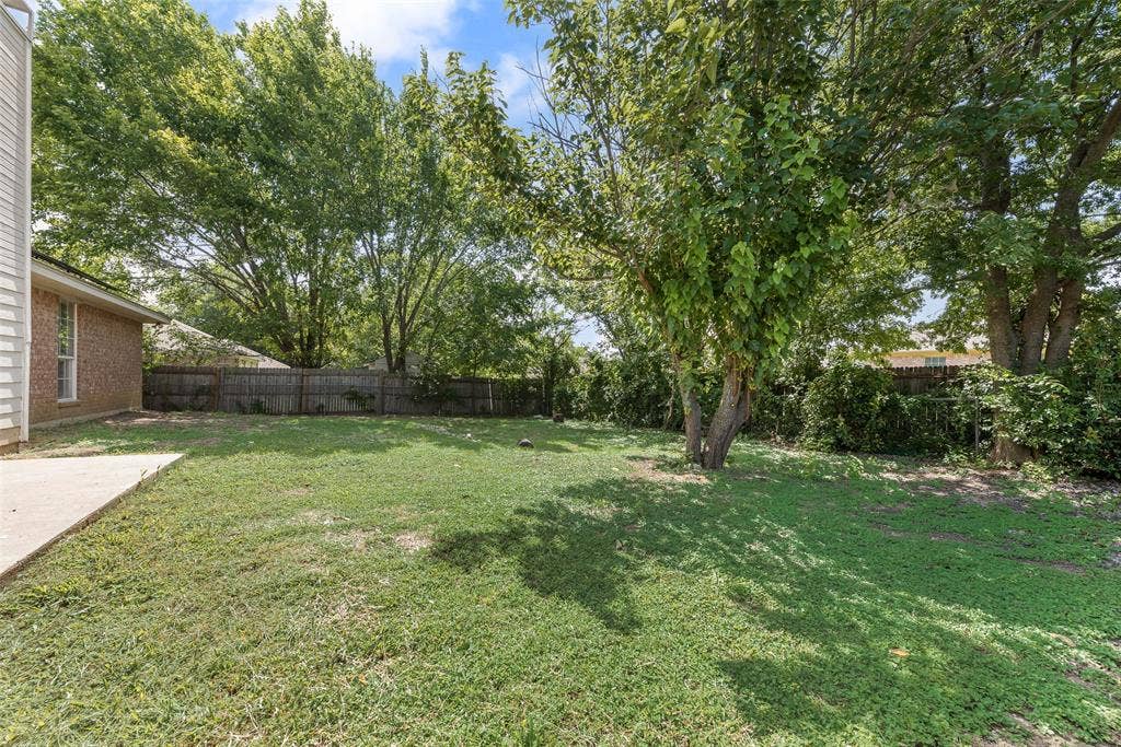 220 Hollywood Drive, Glenn Heights, TX 75154 Expansive green lawn with mature trees providing natural shading, bordered by a wood fence