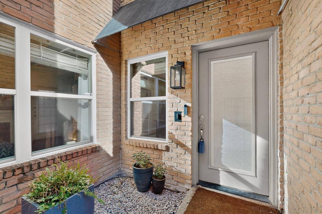 17335 Remington Park Place, Dallas, TX 75252 Brick exterior featuring white-framed windows, an entryway door with an opaque glass insert, and a black exterior wall lantern