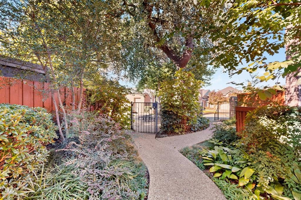 17335 Remington Park Place, Dallas, TX 75252 Paved walkway with lush landscaping, mature trees, and a decorative metal gate