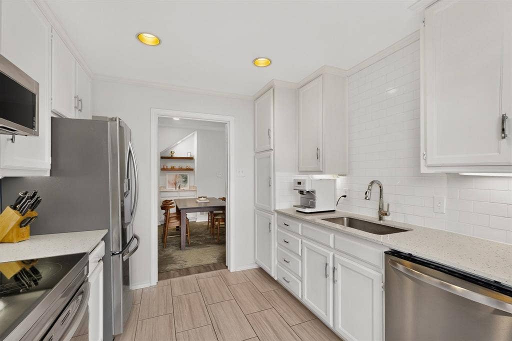 17335 Remington Park Place, Dallas, TX 75252 White cabinetry with crown molding, stainless steel appliances, light-toned countertops, white subway tile backsplash, and wood-finish flooring