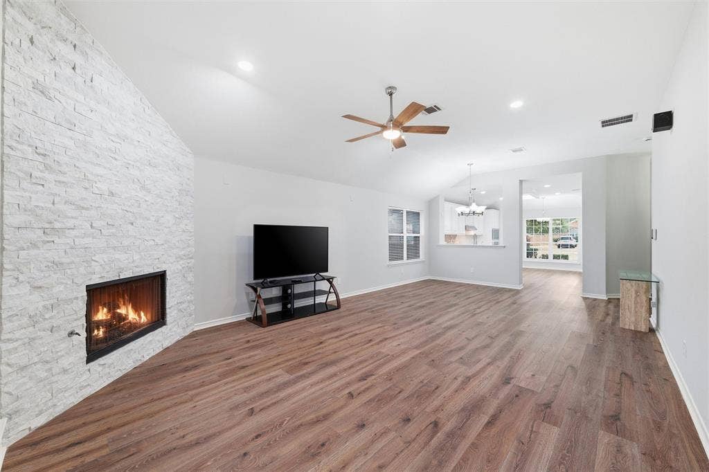 Spacious open-concept living room featuring rich wood-look flooring, soaring ceilings, and a stunning floor-to-ceiling stone fireplace that creates a beautiful focal point year-round.