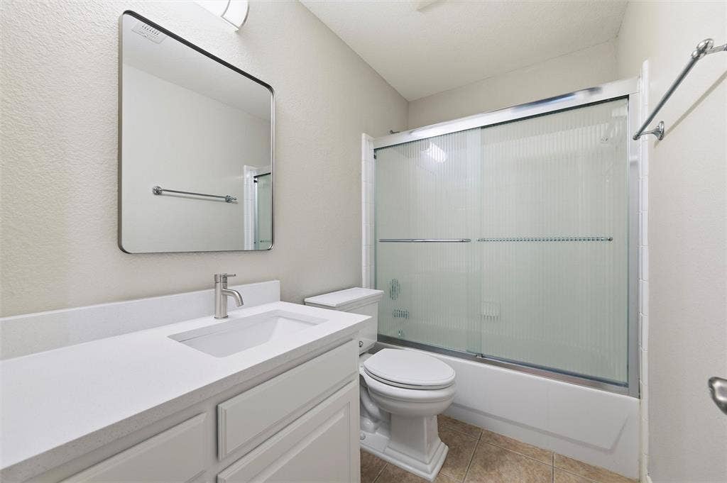 Updated hall bathroom featuring a refreshed vanity with new granite countertop, modern mirror, updated fixtures, and a tub/shower combination with sliding glass enclosure.