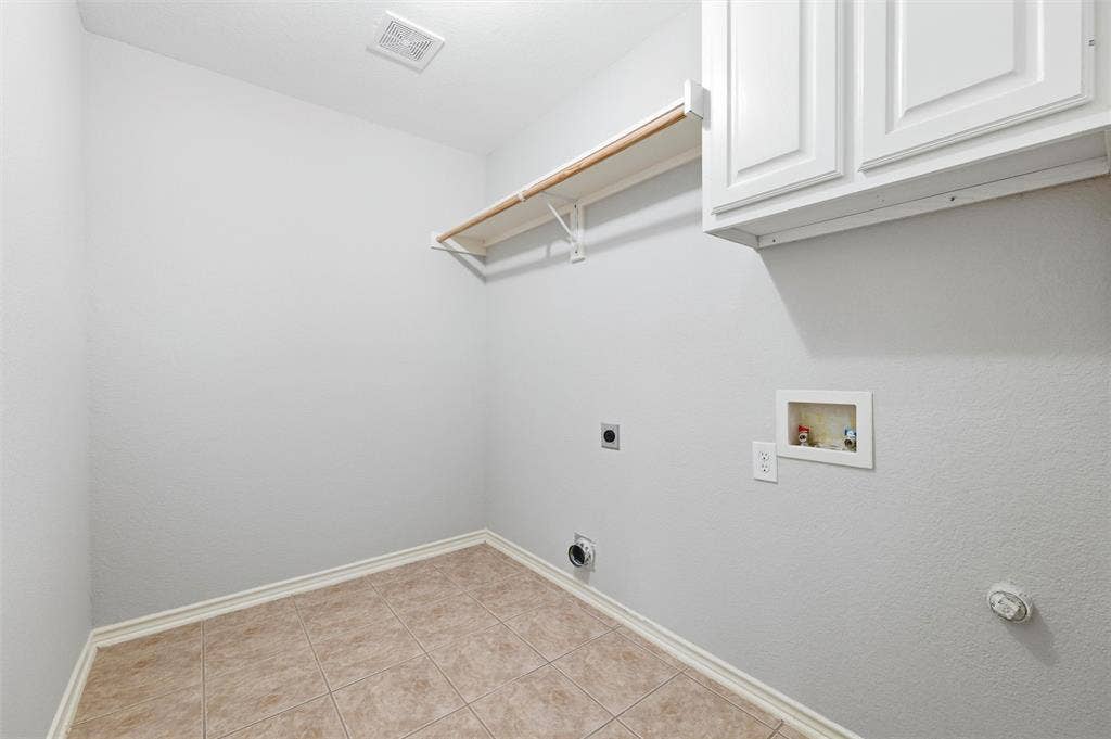 Dedicated laundry room with tile flooring, built-in shelving, and upper cabinetry for convenient storage and organization.