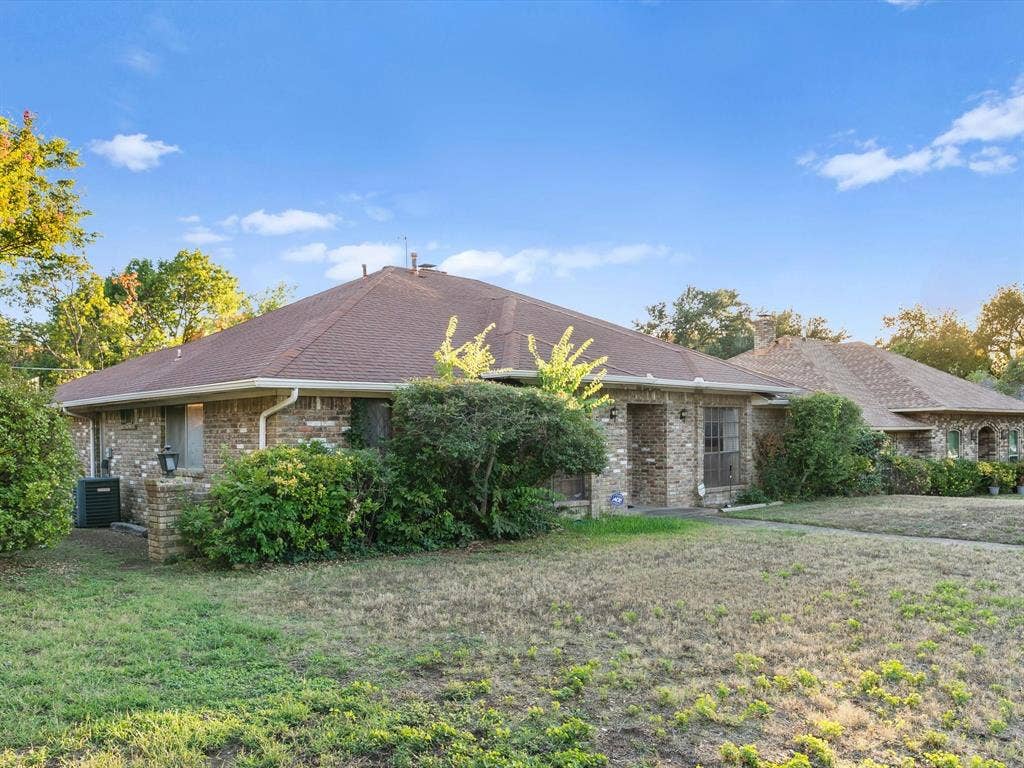 5818 Winding Woods Trail, Dallas, TX 75227 Brick exterior with a brown shingle roof, mature landscaping, and a distinct architectural design
