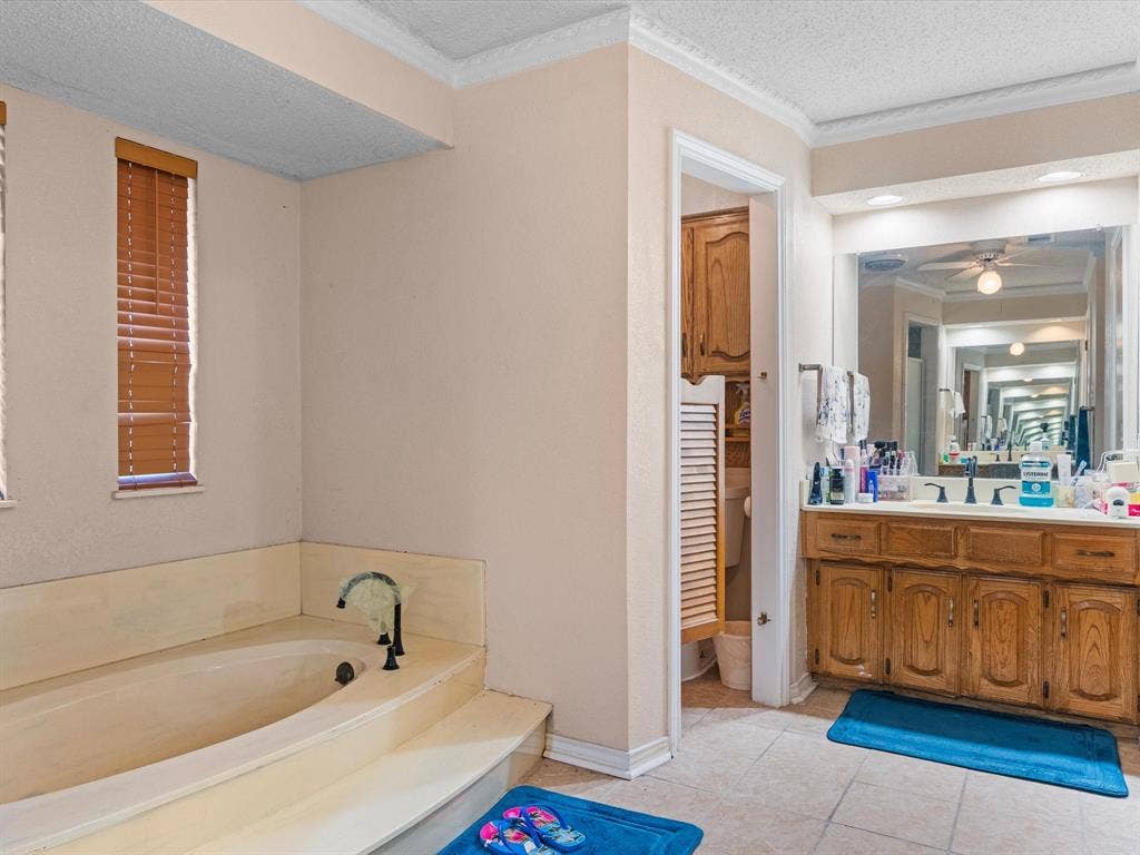 5818 Winding Woods Trail, Dallas, TX 75227 Built-in bathtub with tiered surround, wood-finish blinds, wood vanity with integrated sink, large wall mirror, and tile flooring