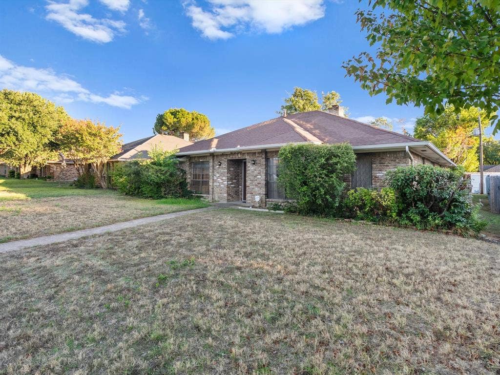 5818 Winding Woods Trail, Dallas, TX 75227 Brick exterior with a dark-pitched roof, featuring established shrubs.