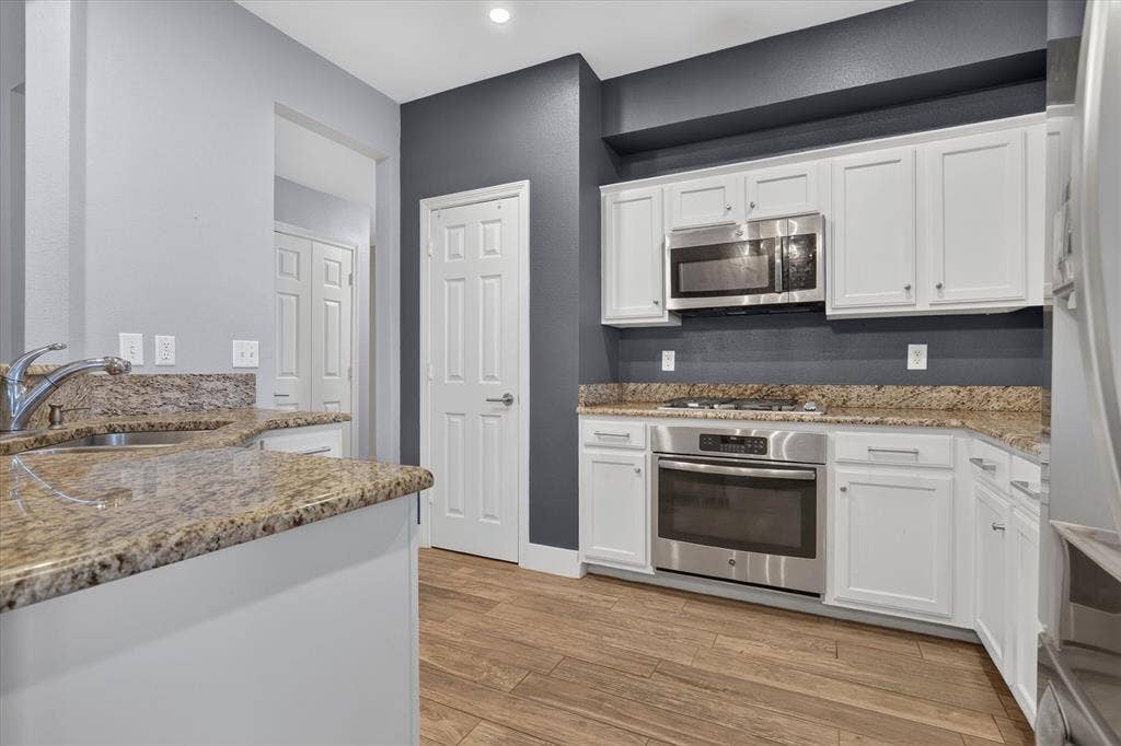 1825 Bachman Court, Plano, TX 75075 Kitchen featuring white cabinetry, stone-surface countertops, wood-finish flooring, and built-in stainless steel appliances