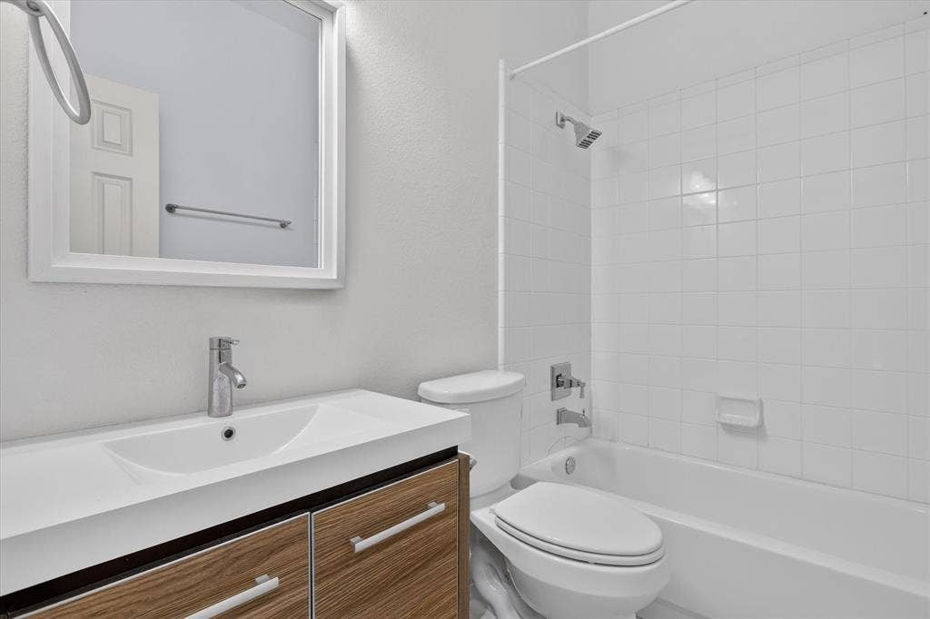 1825 Bachman Court, Plano, TX 75075 Bathroom featuring a vanity with a wood-finish cabinet and integrated sink, a framed wall mirror, a ceramic tile tub surround, and polished chrome fixtures