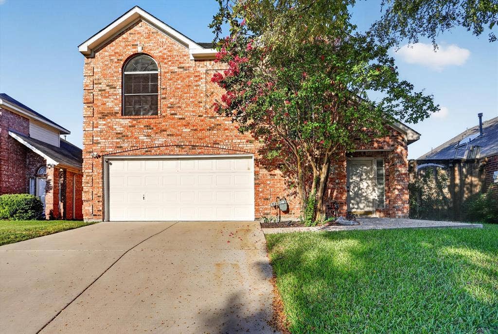 1825 Bachman Court, Plano, TX 75075 Multi-story brick exterior featuring a prominent arched window, two-car garage, concrete driveway, and front lawn landscaping