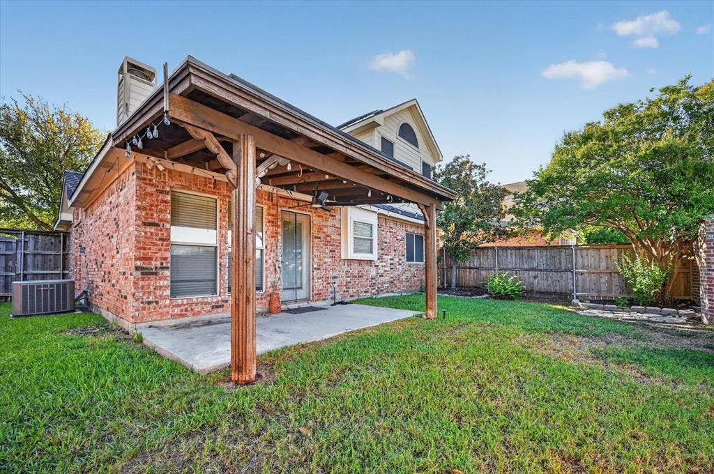 1825 Bachman Court, Plano, TX 75075 Rear brick elevation with a covered patio, concrete slab, wood privacy fencing, and a mature tree