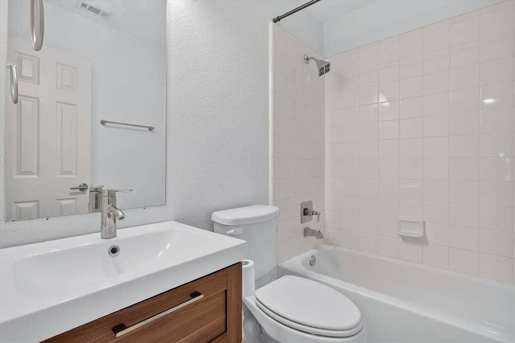 1825 Bachman Court, Plano, TX 75075 Bathroom featuring a wood-finish floating vanity, rectangular sink with a chrome faucet, large frameless wall-mounted mirror, and a tub-shower combination with white tiled surround