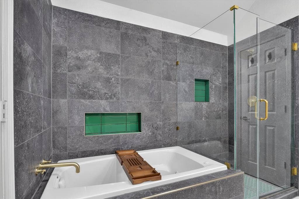 1825 Bachman Court, Plano, TX 75075 Large soaking tub featuring gold-tone hardware, dark stone-finish wall tiling, glass-enclosed shower with gold-tone fixtures, and dual recessed wall niches