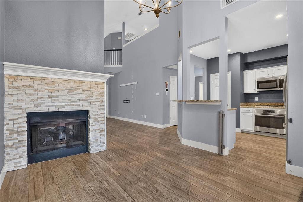 1825 Bachman Court, Plano, TX 75075 Floor-to-ceiling fireplace with stacked-stone facade, wood-finish flooring, soaring ceilings, kitchen featuring white cabinetry and stone countertops, and overhead decorative lighting
