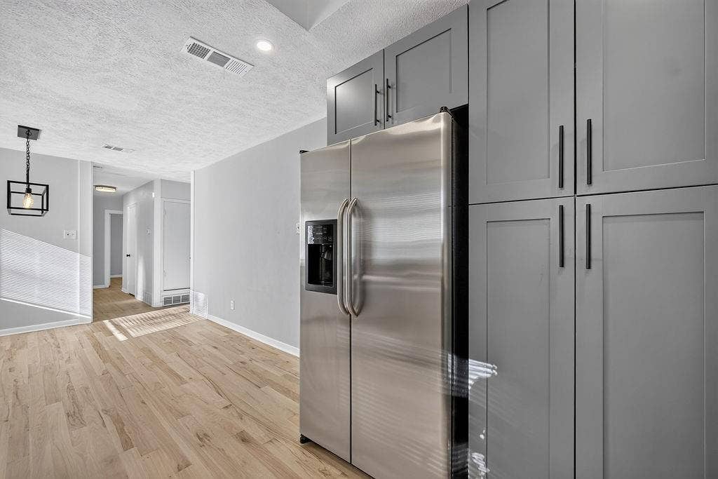 9112 Clearwater Drive, Dallas, TX 75243 Full-height grey cabinetry with matte black hardware, stainless steel refrigerator, recessed lighting, wood-finish flooring, and a modern ceiling light fixture