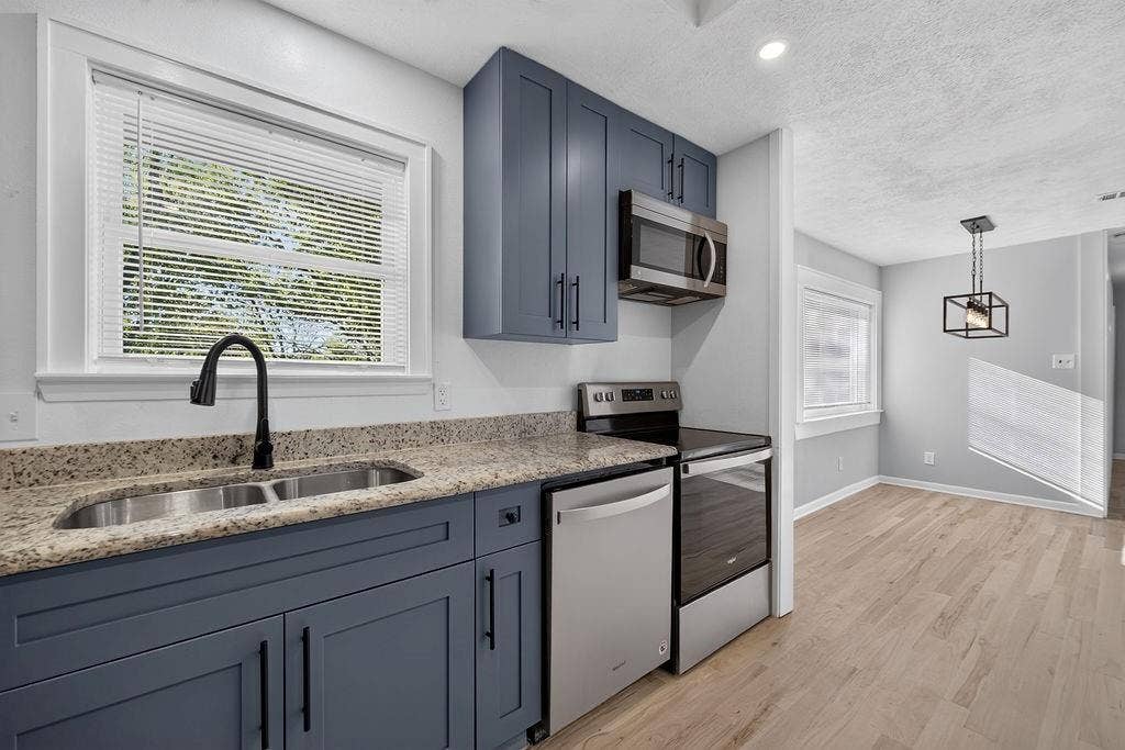 9112 Clearwater Drive, Dallas, TX 75243 Kitchen featuring blue shaker cabinetry, granite-style countertops, stainless steel appliances, and a double basin sink with a matte black faucet