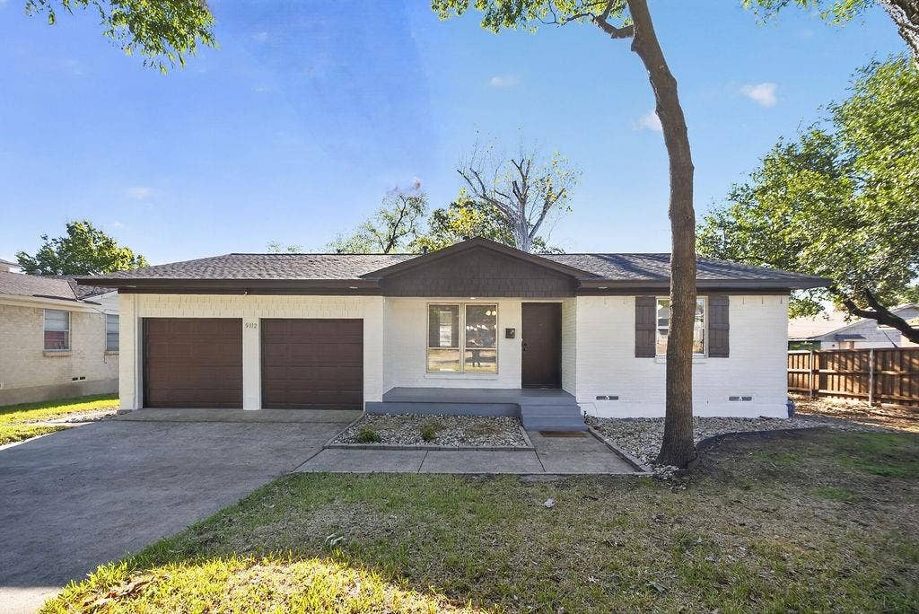 9112 Clearwater Drive, Dallas, TX 75243 White brick exterior with a dark brown roof and matching two-car garage doors