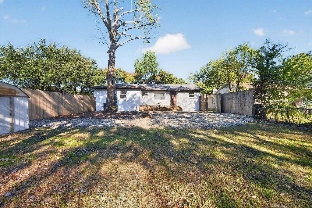 9112 Clearwater Drive, Dallas, TX 75243 Expansive backyard featuring a manicured lawn, established tree, and a wooden privacy fence
