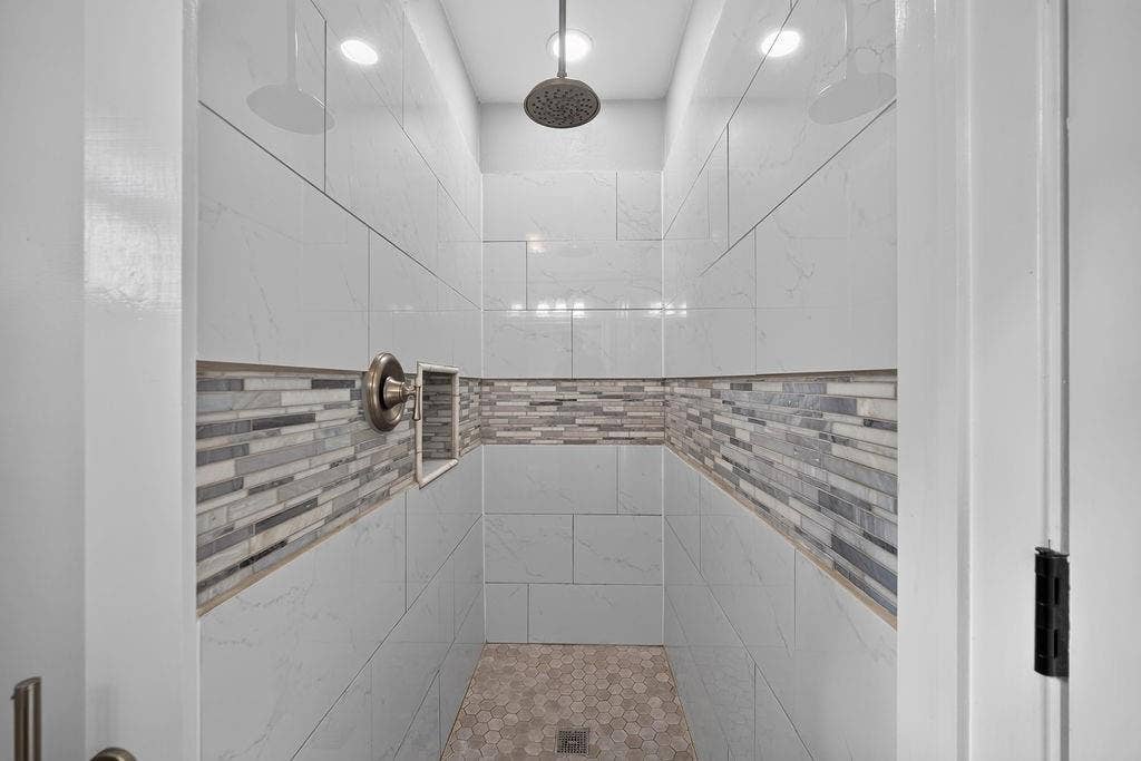 9112 Clearwater Drive, Dallas, TX 75243 Spacious shower featuring full-height light-toned tile, decorative mosaic tile band, a built-in niche, and a rain shower head
