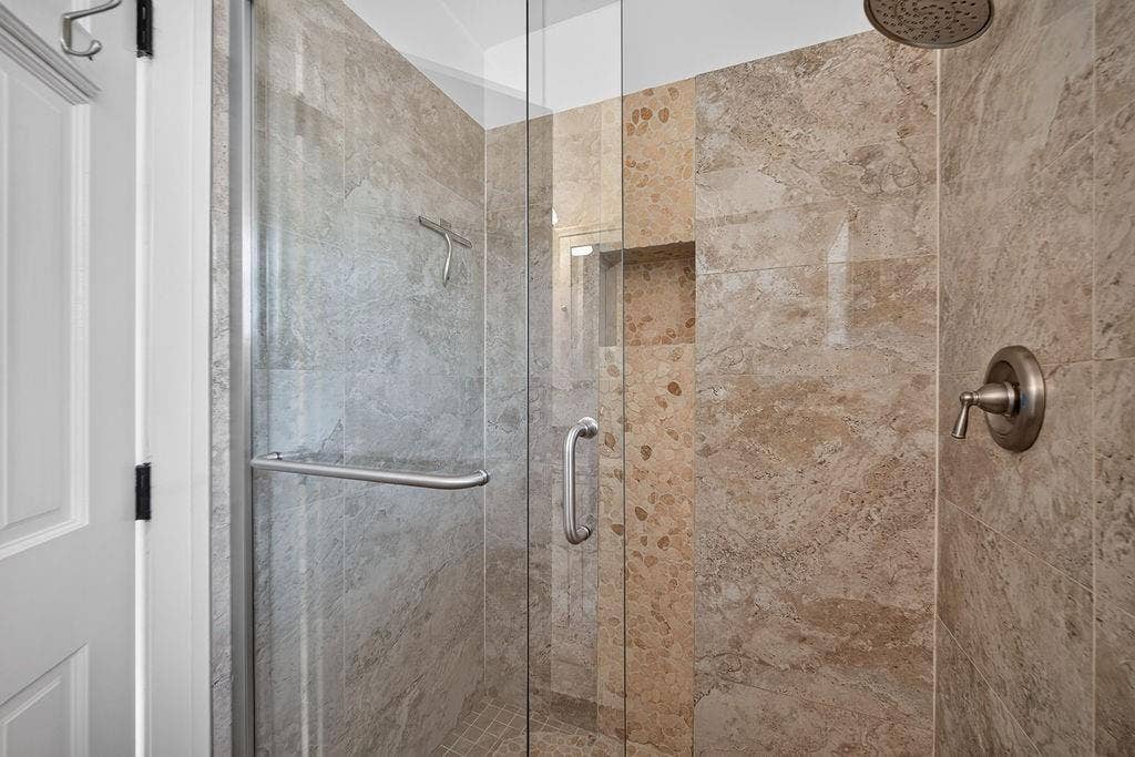 9112 Clearwater Drive, Dallas, TX 75243 Glass-enclosed shower featuring natural stone-finish tiling, a built-in shower niche, and a rain showerhead