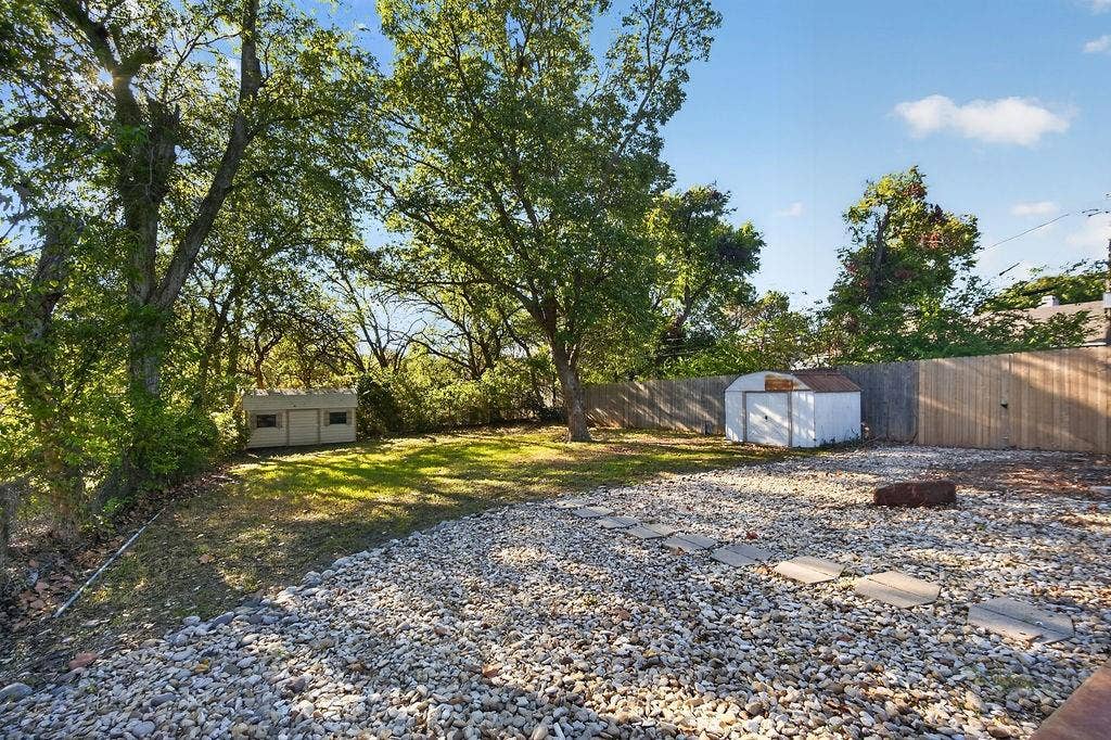 9112 Clearwater Drive, Dallas, TX 75243 Expansive backyard featuring a gravel patio with stepping stones, a wooden privacy fence, mature trees, and a storage shed