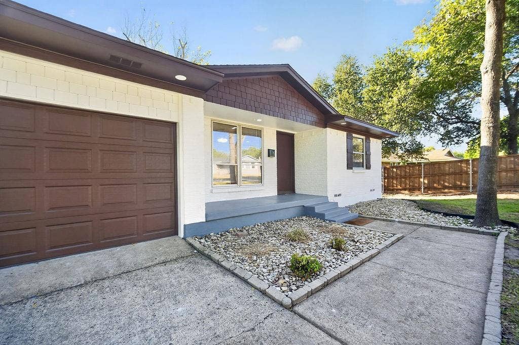 9112 Clearwater Drive, Dallas, TX 75243 White brick exterior with a brown garage door, front entry porch, and partial shingle siding