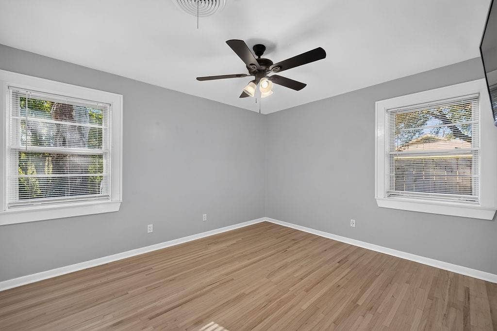 9112 Clearwater Drive, Dallas, TX 75243 Spacious room featuring light gray walls, wood-finish flooring, two windows with blinds, and a ceiling fan with integrated lighting
