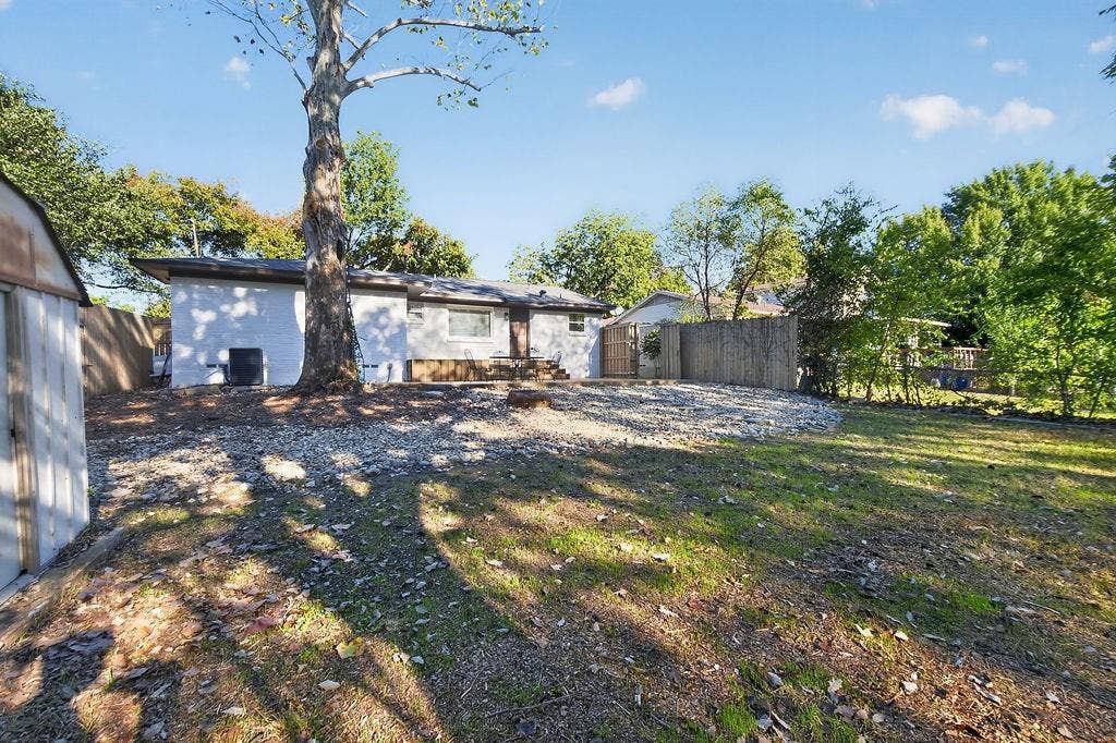 9112 Clearwater Drive, Dallas, TX 75243 Expansive backyard featuring a large mature tree, gravel landscaping, and a wooden privacy fence