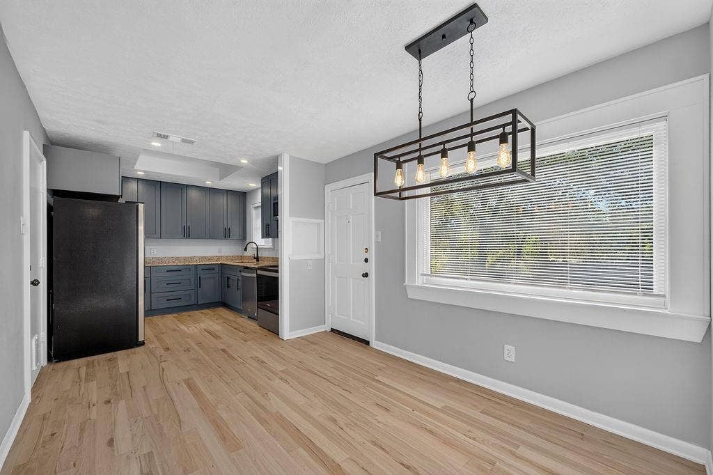 9112 Clearwater Drive, Dallas, TX 75243 Wood-finish flooring, modern linear chandelier, gray wall paint, white trim, and a kitchen featuring blue cabinetry and light-colored countertops